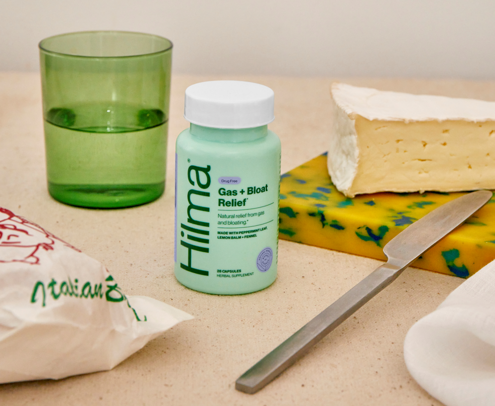 Gas + Bloat Relief bottle next to a baguette, brie cheese, and a glass of water