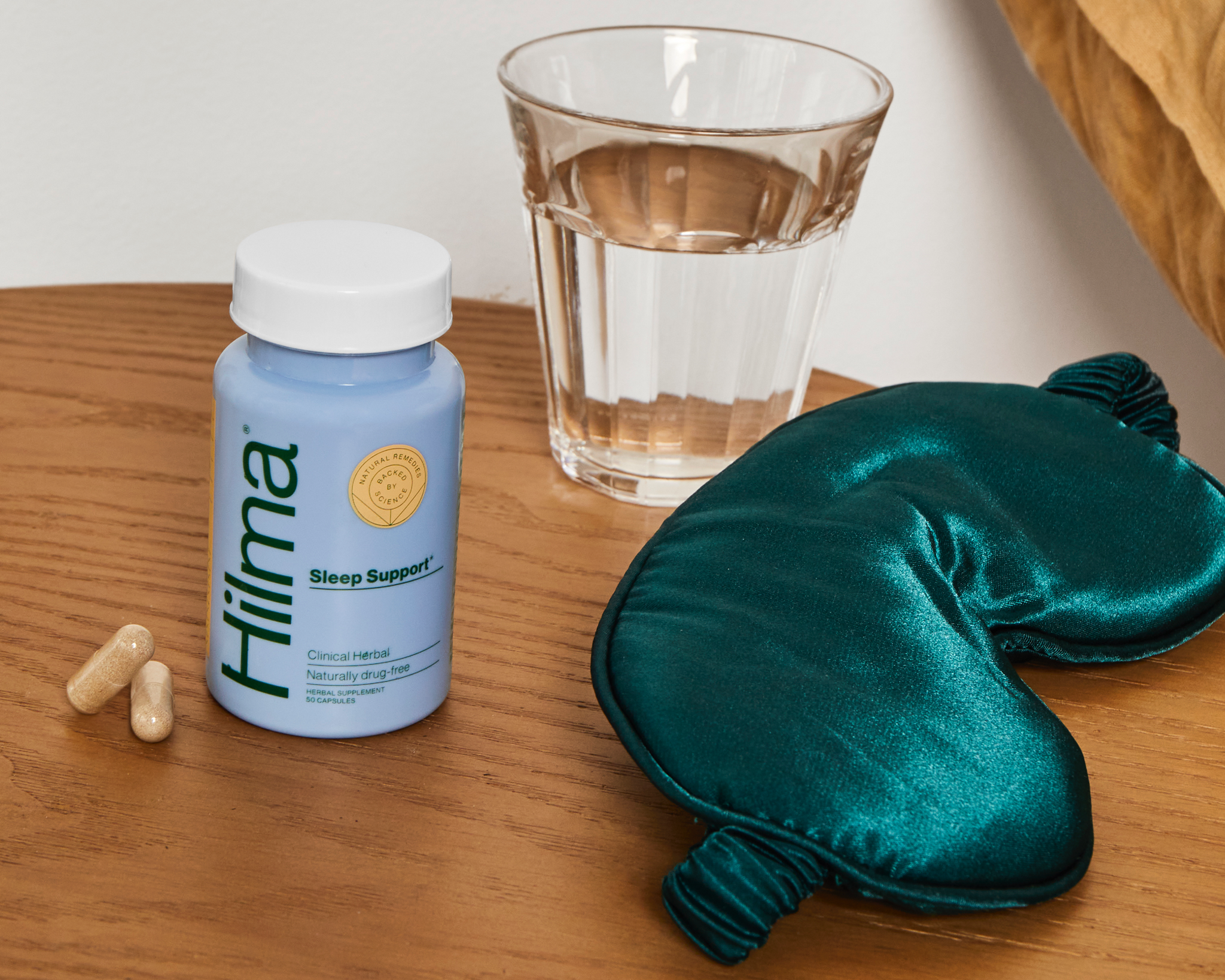 Sleep Support bottle & 2 pills on a nightstand next to an eye mask and glass of water