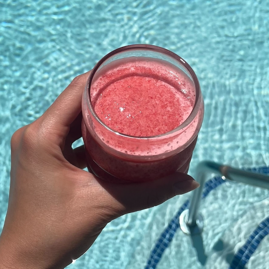 hand holding pink smoothie in a glass over a pool