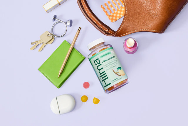 Brown leather pouch with various items on a light purple background