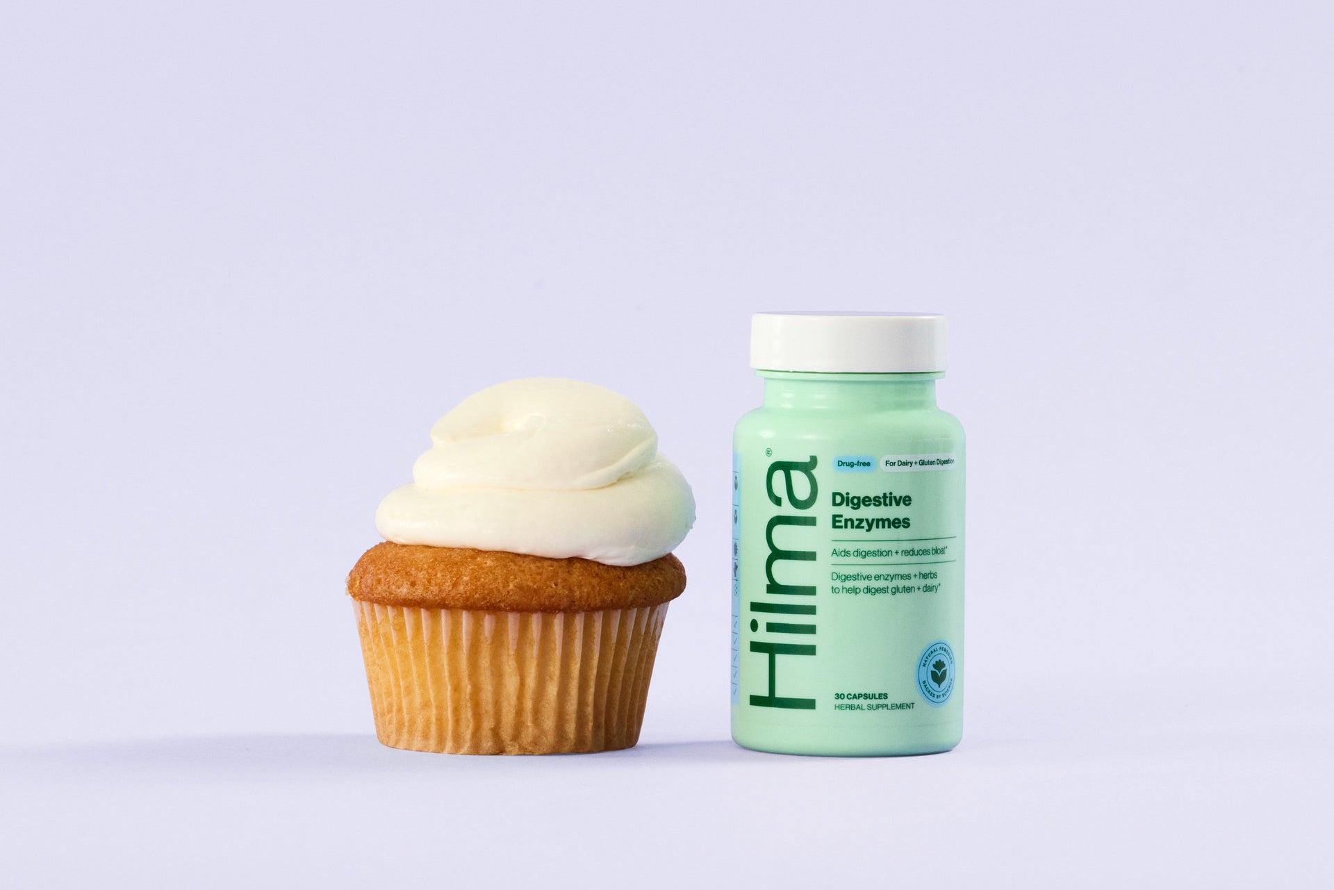 Bottle of Hilma enzymes next to a cupcake on a light purple background