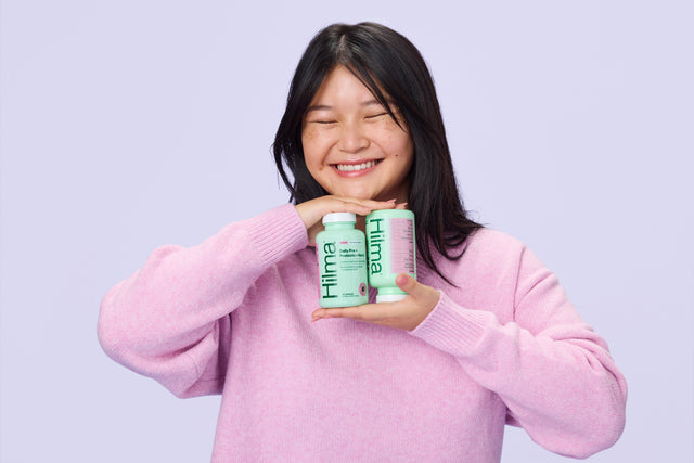 Person holding two bottles of Hilma probiotic with a plain background