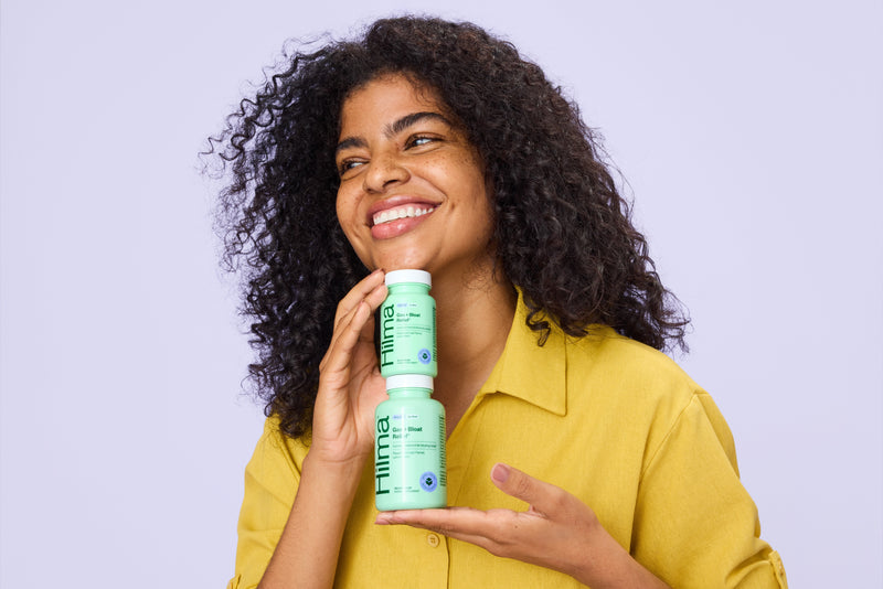 Woman holding a stack of Hilma Gas + Bloat products against a light purple background

