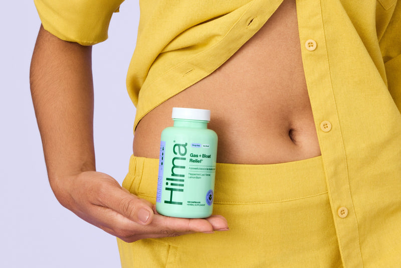 Person holding a bottle labeled 'Hilma' against a light purple background