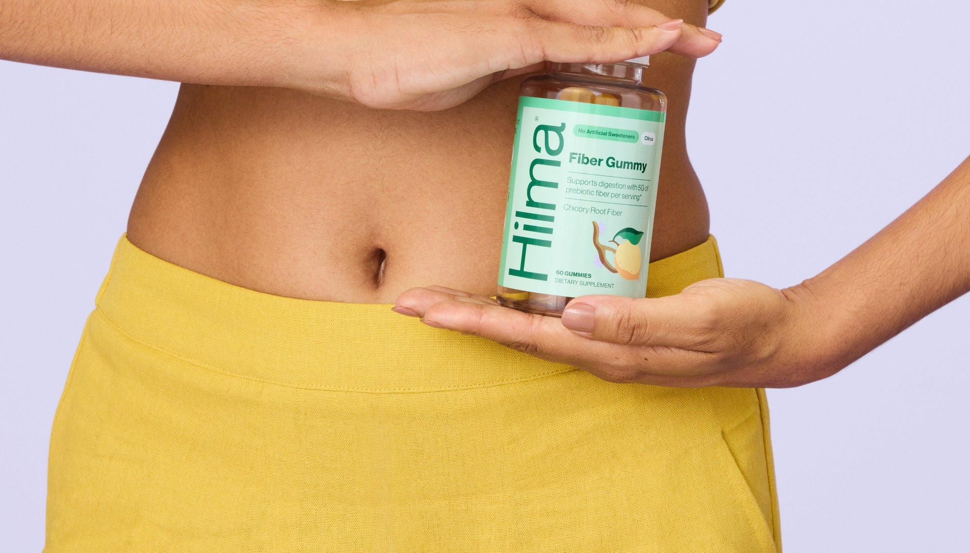 Person holding a bottle of Hima Fiber gummies against a light purple background