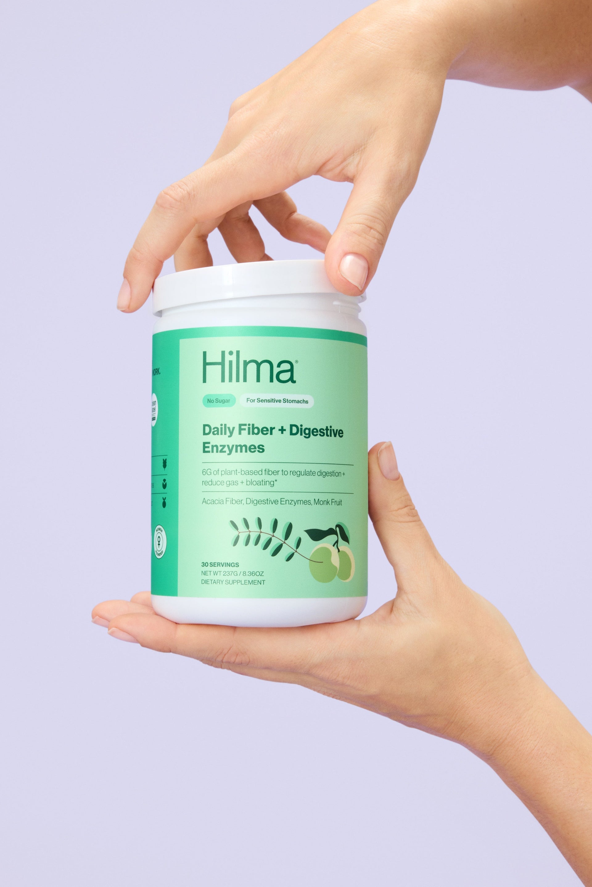 Person holding a container of Hilma Daily Fiber + Digestive Enzymes on a light purple background