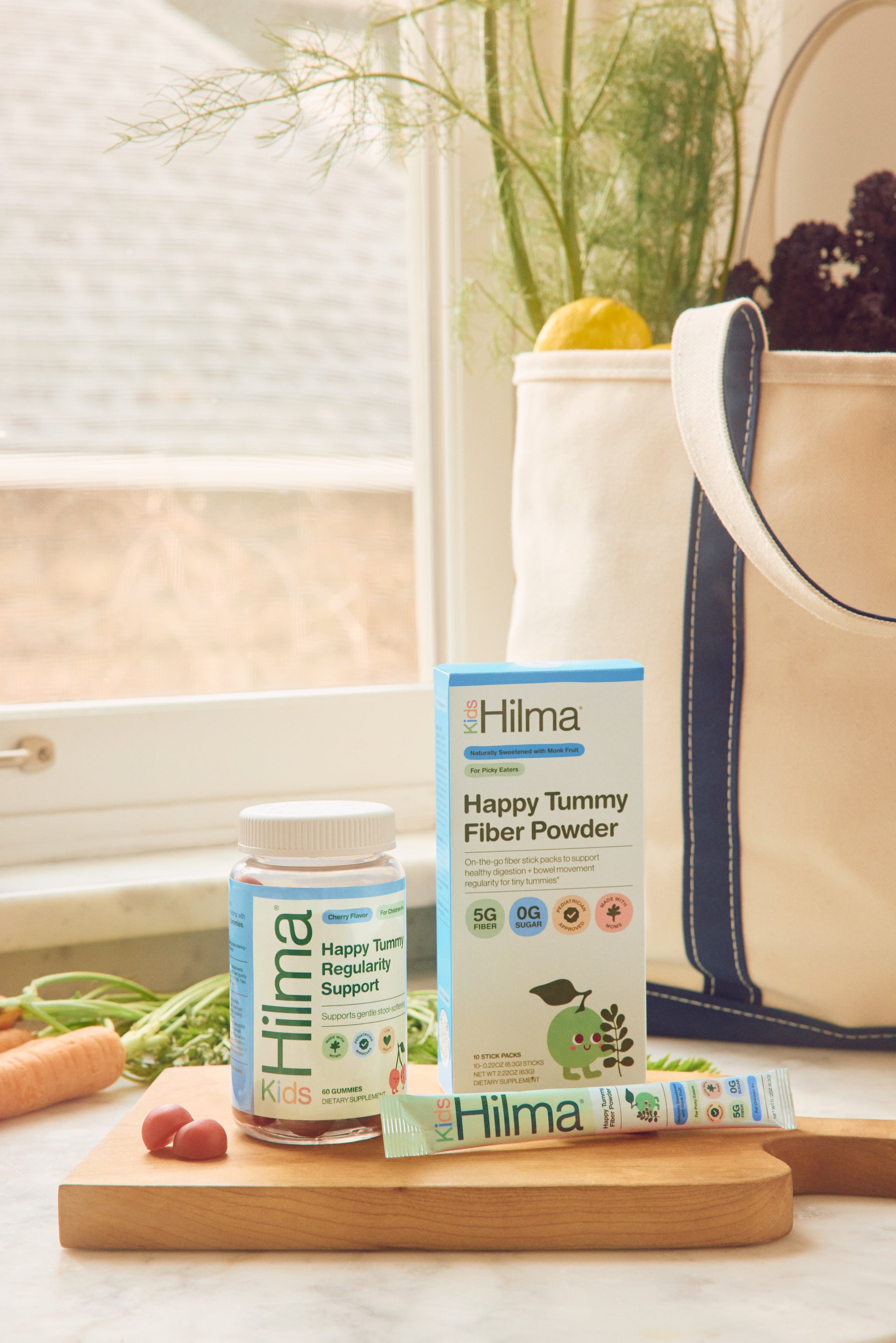 Hilma Happy Tummy Fiber Powder packaging on a kitchen counter with a window and fruit in the background.