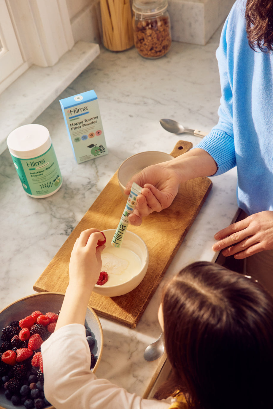 Person feeding a child with a spoon in a kitchen setting, with Huma product visible.
