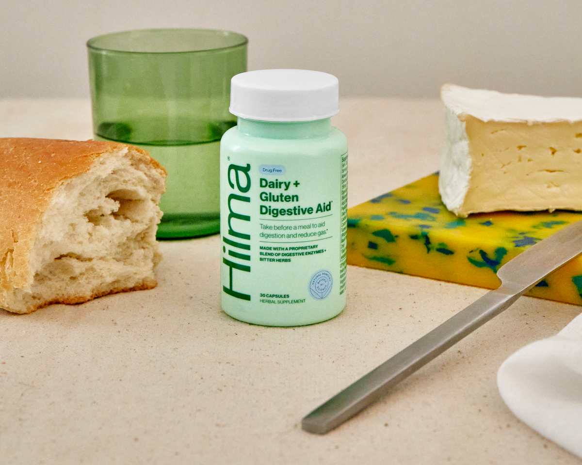 Dairy + Gluten Digestive Aid bottle next to brie cheese, a baguette, and a glass of water