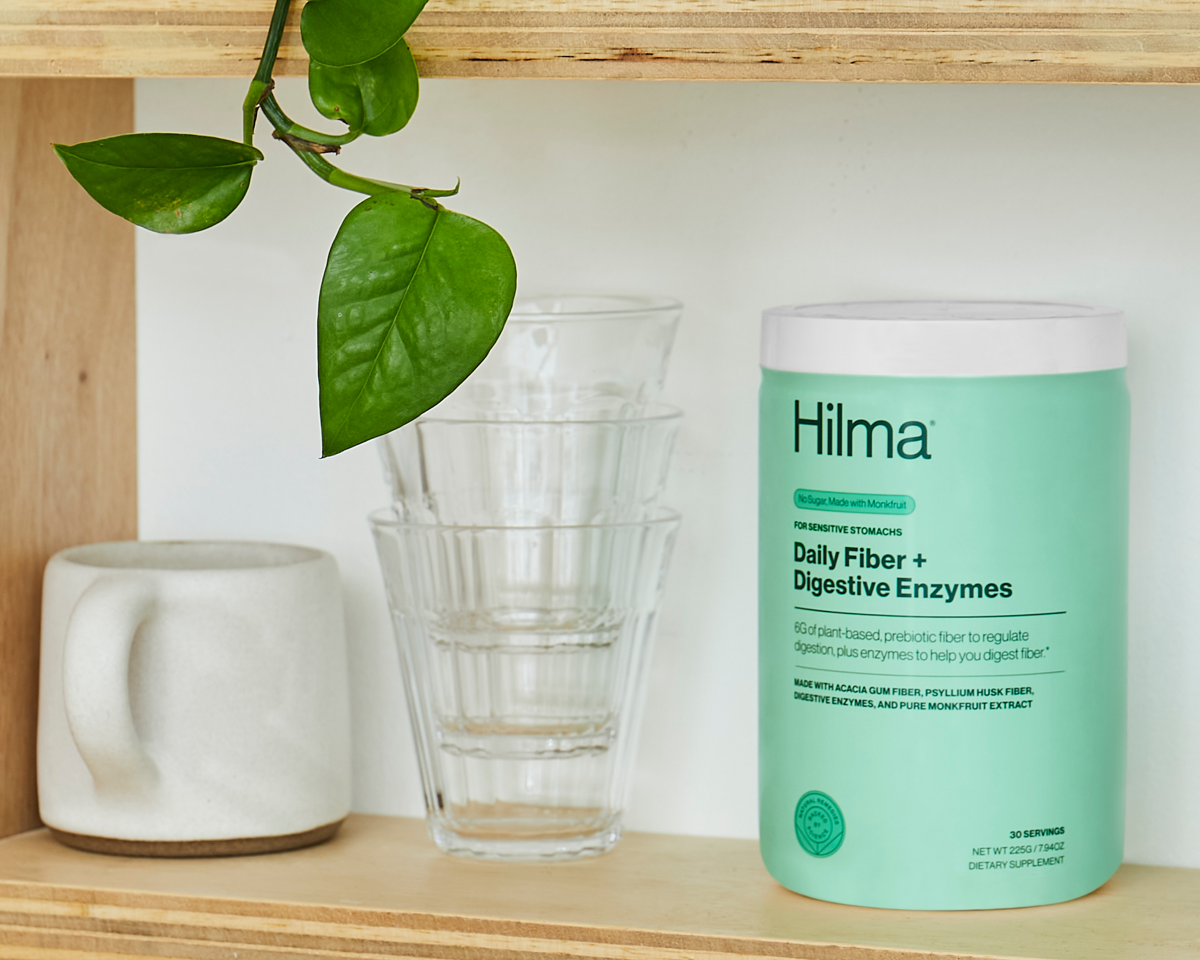 Daily Fiber + Digestive Enzymes on shelf with water glasses and plant in background